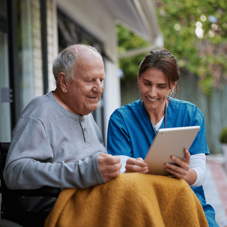 Caregiver showing tablet to smiling elderly man