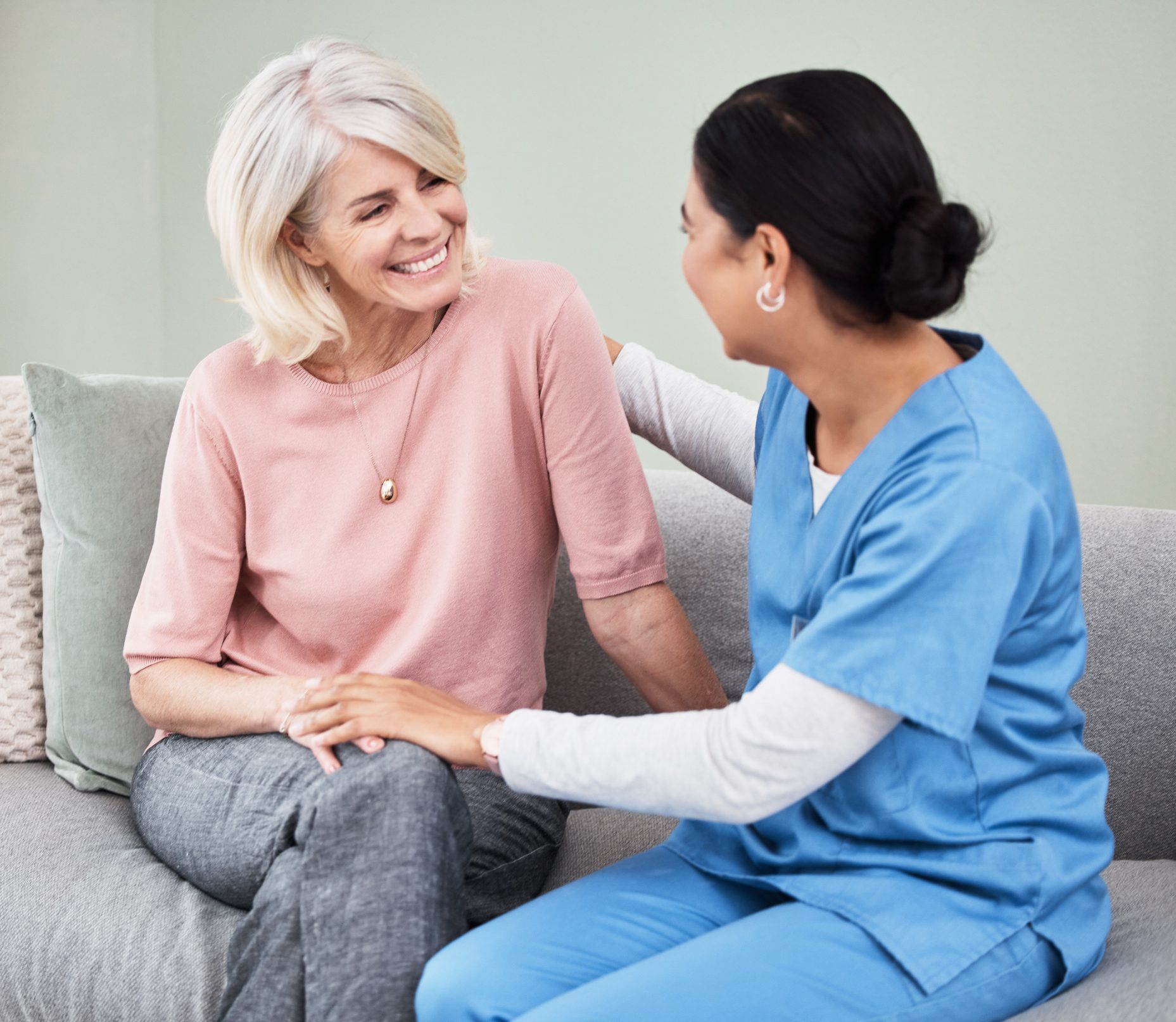 Smiling caregiver comforting senior woman on couch