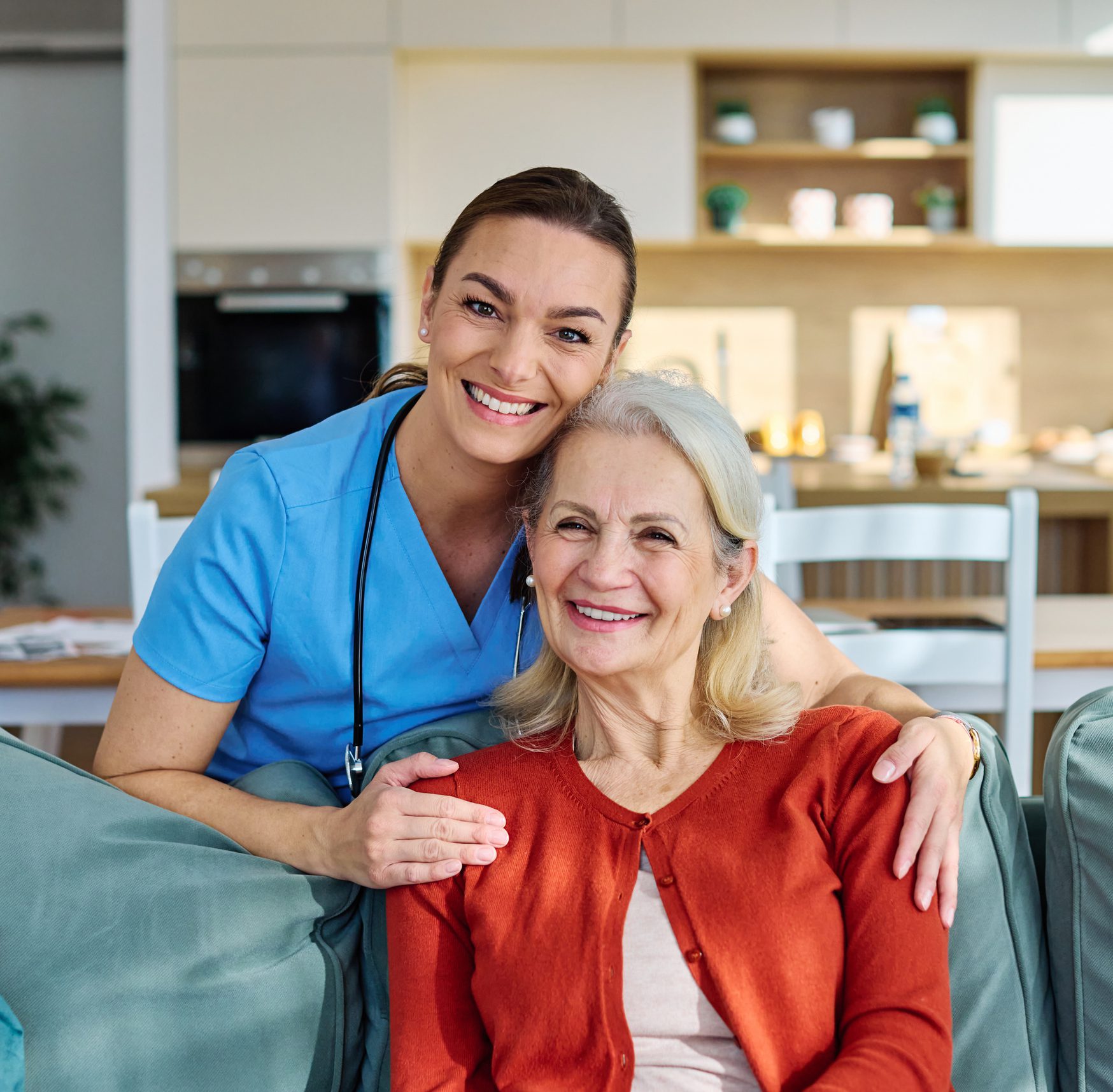 Home caregiver embraces smiling senior woman on couch