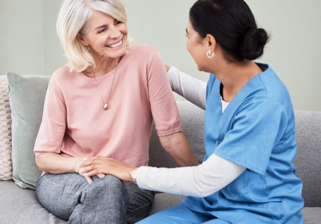 Smiling caregiver comforting senior woman on couch