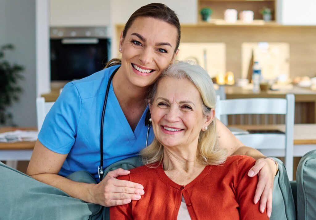 Home caregiver embraces smiling senior woman on couch